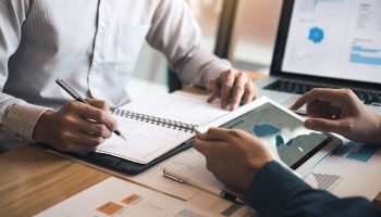 Two business partnership coworkers discussing a financial planning graph and company during a budget meeting in office room.